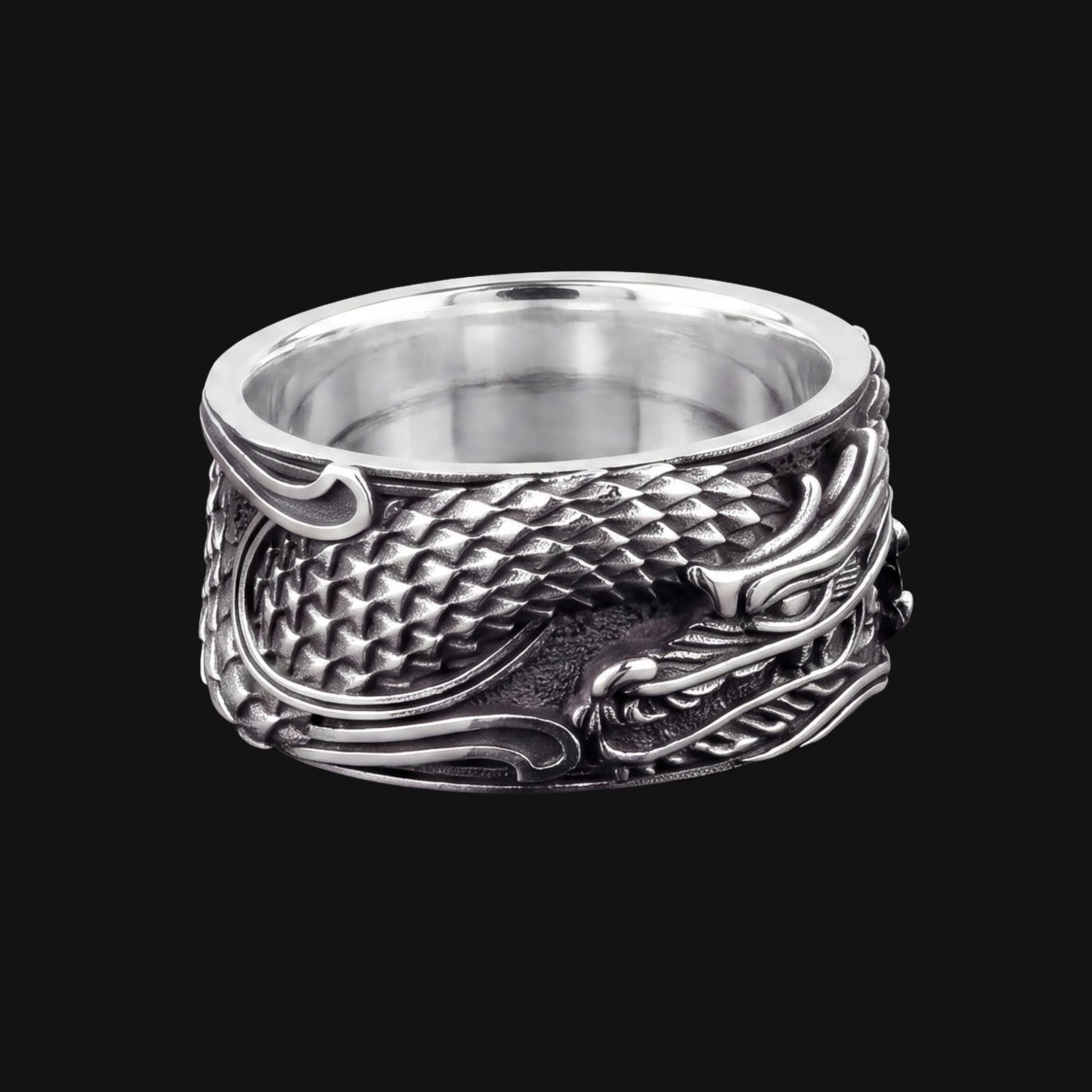 A wide silver ring featuring an embossed dragon design with detailed scales and flowing claws, shown against a solid black background.