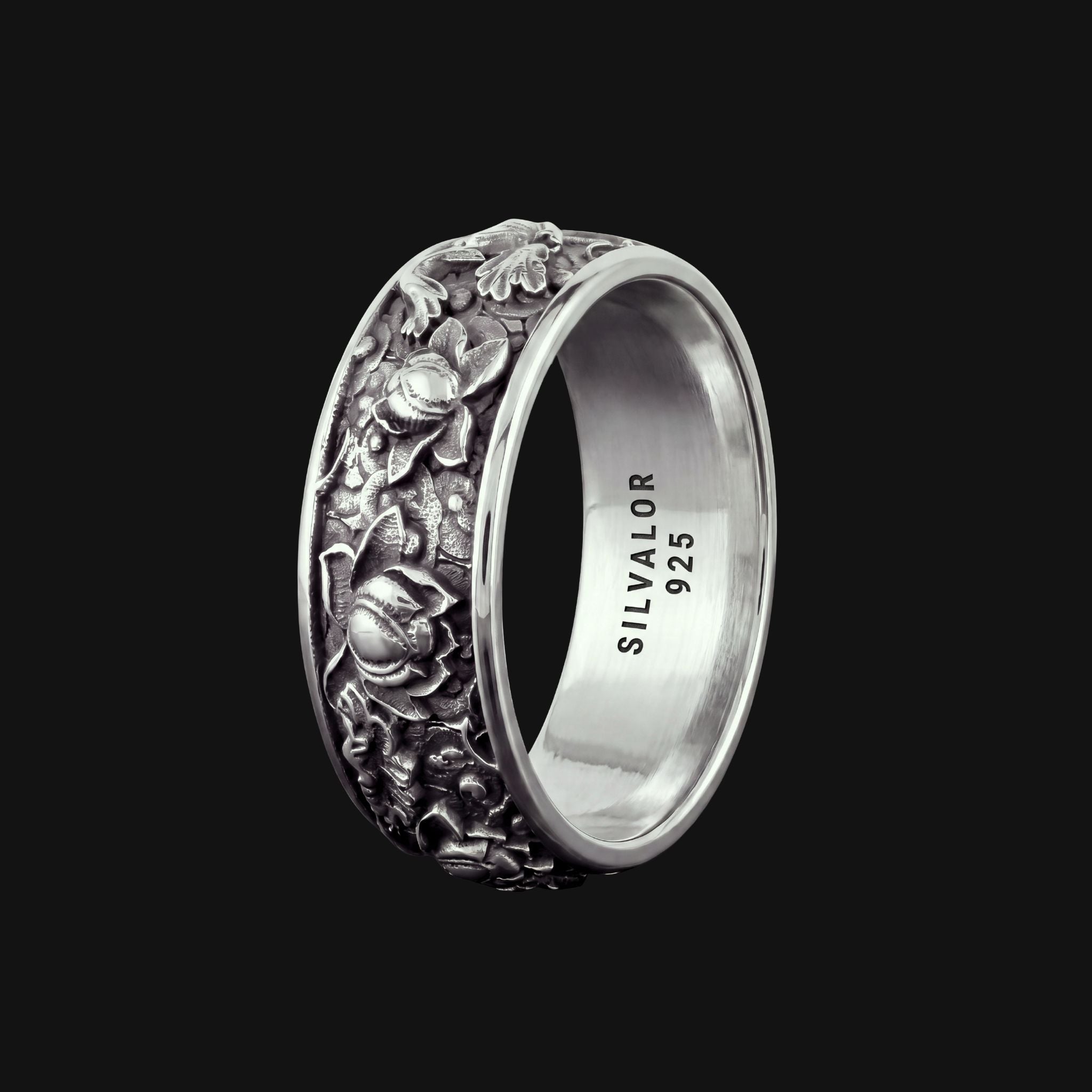 A silver band ring featuring an intricate floral relief pattern on the exterior, with 'SILVALOR 925' engraved on the polished interior, set against a solid black background.