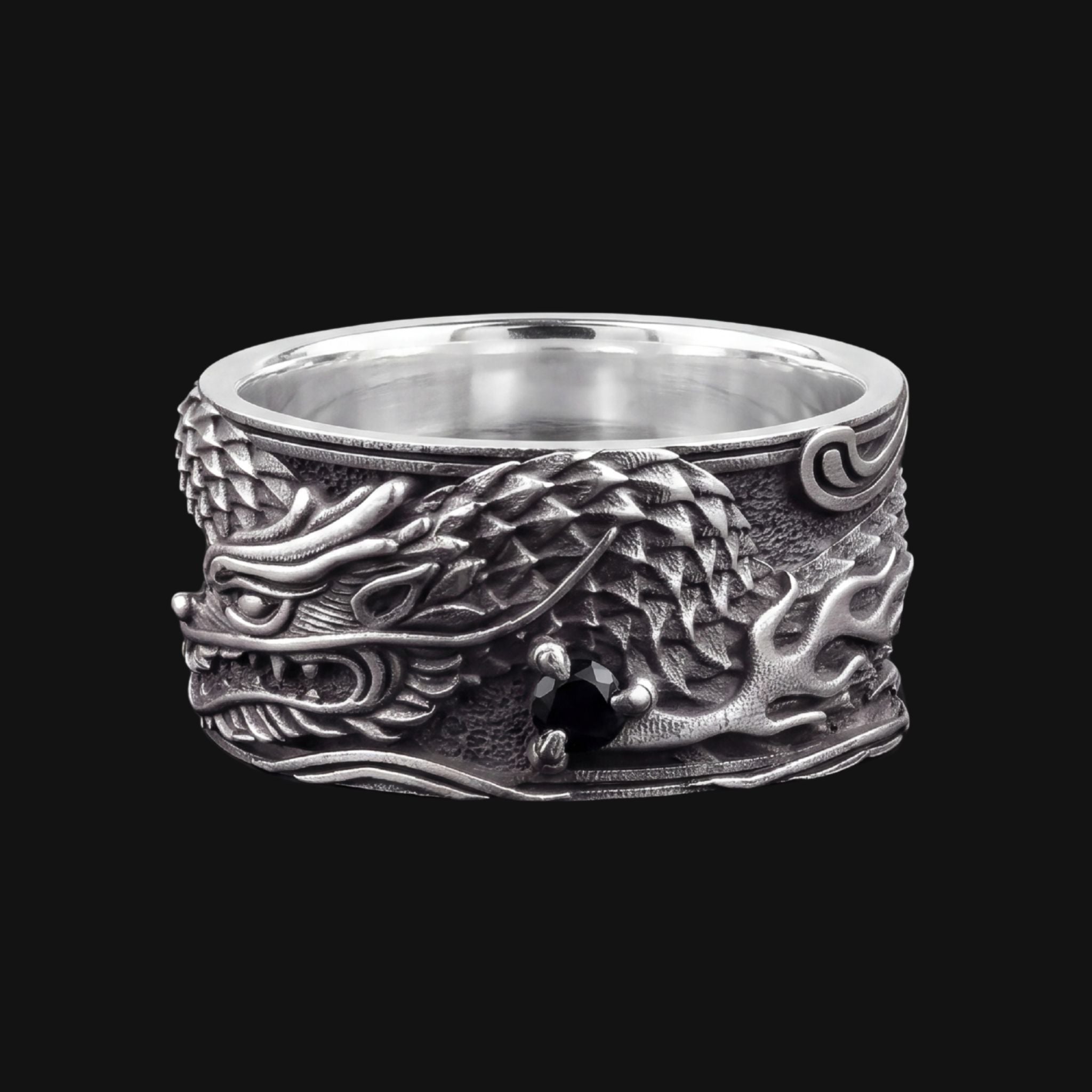 A wide sterling silver ring featuring a highly detailed, raised dragon design with textured scales and a polished inner band, shown against a solid black background.