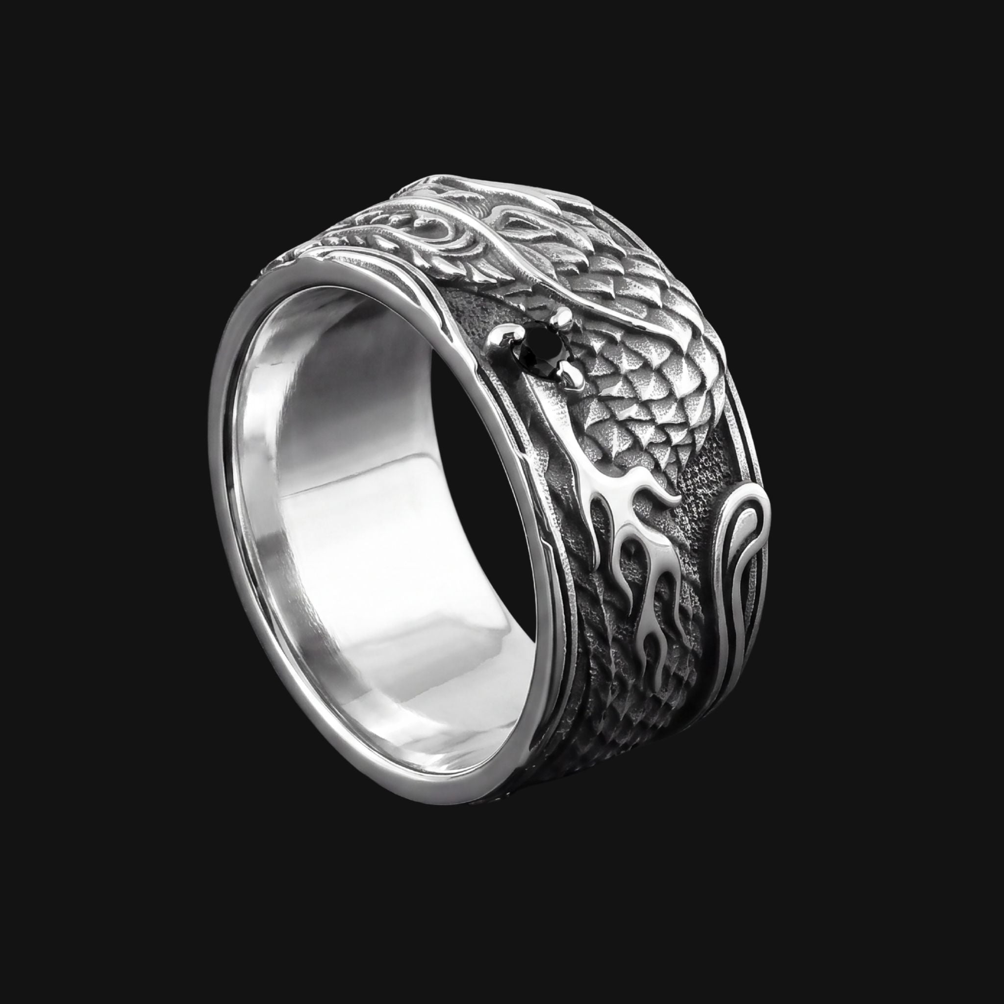 A polished silver ring featuring an embossed dragon design with textured scales and a small black stone accent, set against a solid black background.